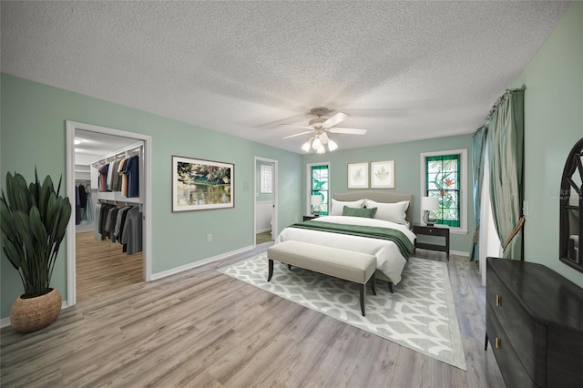 bedroom with light wood-type flooring, a spacious closet, ceiling fan, a textured ceiling, and a closet