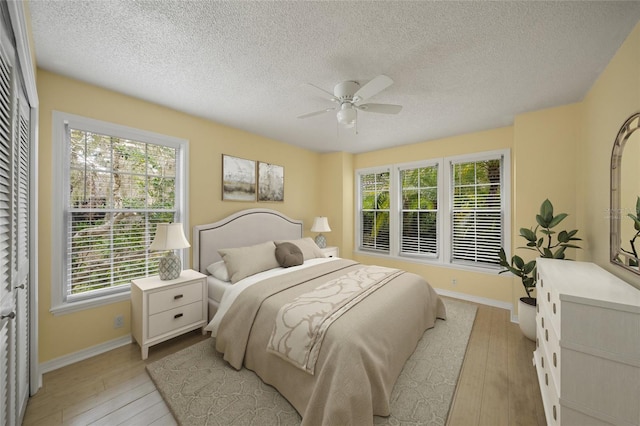 bedroom with baseboards, ceiling fan, a textured ceiling, and light wood finished floors