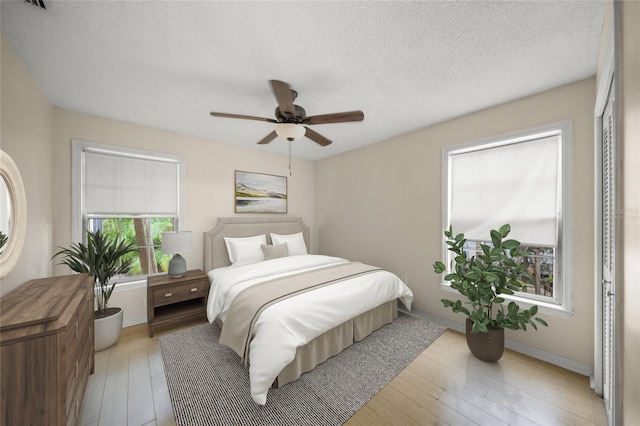 bedroom with a ceiling fan, light wood-type flooring, a textured ceiling, and baseboards