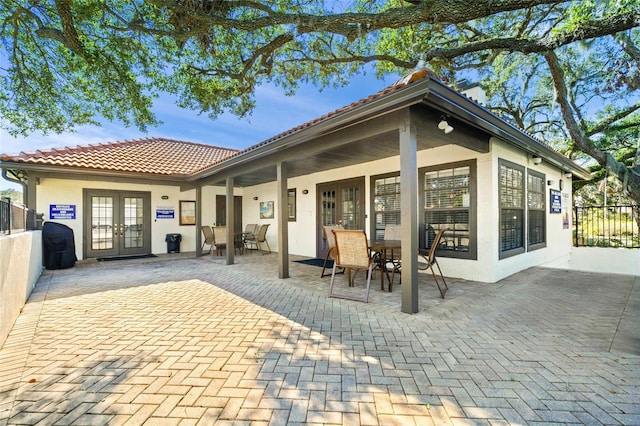 rear view of house featuring french doors, a tile roof, fence, and stucco siding