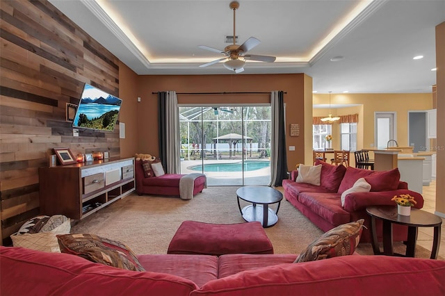 carpeted living room featuring ceiling fan with notable chandelier, wooden walls, and a raised ceiling