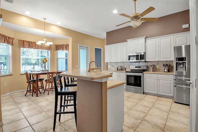 kitchen with appliances with stainless steel finishes, a breakfast bar, white cabinetry, decorative backsplash, and a kitchen island with sink