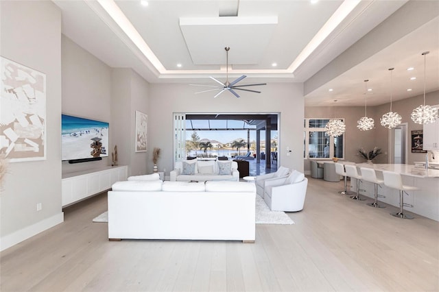 living room with a chandelier, a raised ceiling, a high ceiling, and light wood-type flooring