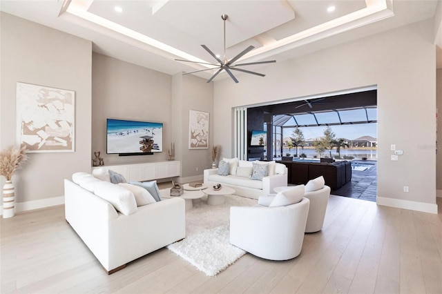 living room with a raised ceiling, a towering ceiling, and light hardwood / wood-style flooring