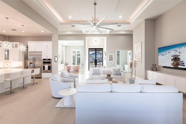 living room featuring a tray ceiling, a chandelier, light hardwood / wood-style floors, and a high ceiling