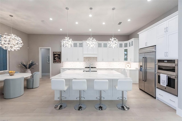 kitchen with stainless steel appliances, an island with sink, pendant lighting, and white cabinets