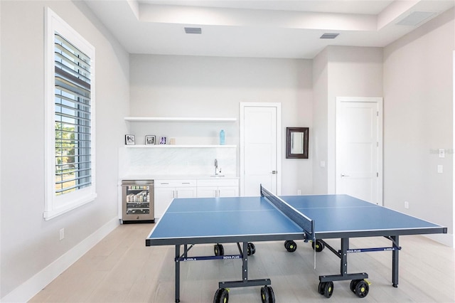 rec room with wine cooler, light wood-type flooring, and a tray ceiling