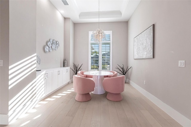 dining area with a tray ceiling, a chandelier, and light hardwood / wood-style flooring