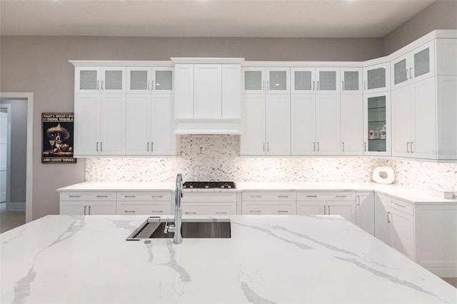 kitchen featuring light stone counters, sink, white cabinetry, and backsplash