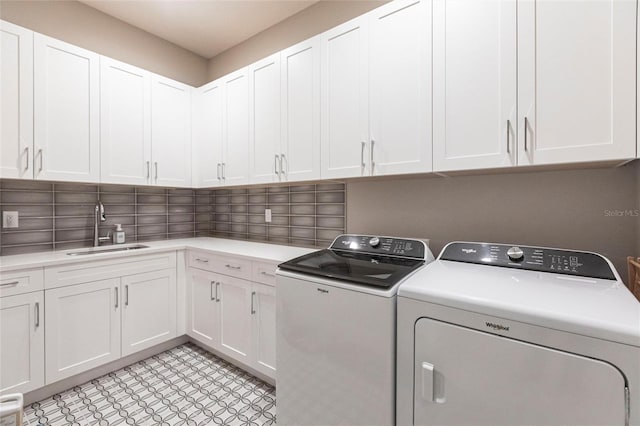 clothes washing area with separate washer and dryer, sink, and cabinets