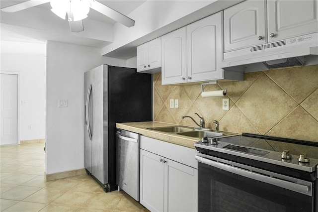 kitchen with appliances with stainless steel finishes, sink, white cabinets, backsplash, and light tile patterned floors