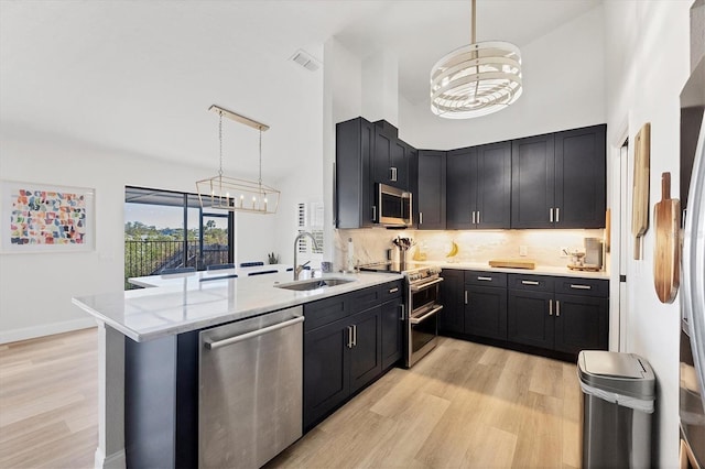 kitchen featuring sink, hanging light fixtures, appliances with stainless steel finishes, kitchen peninsula, and a towering ceiling