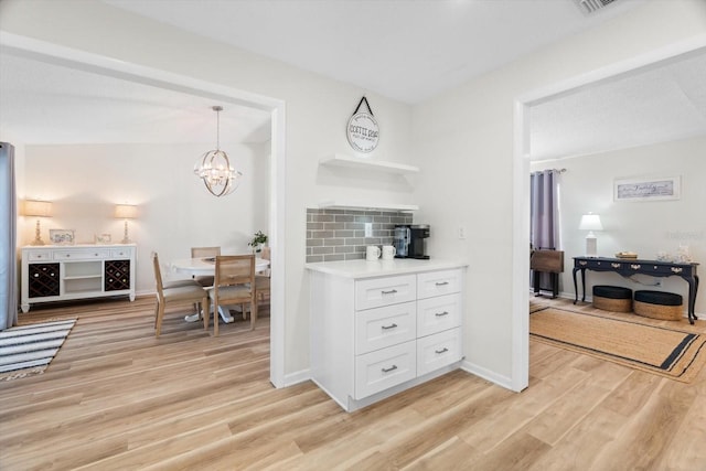 kitchen with pendant lighting, backsplash, white cabinetry, and light hardwood / wood-style floors