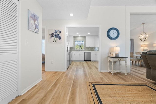 corridor featuring an inviting chandelier, vaulted ceiling, and light wood-type flooring