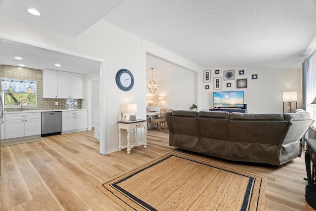 living room featuring vaulted ceiling, an inviting chandelier, light hardwood / wood-style floors, and a textured ceiling