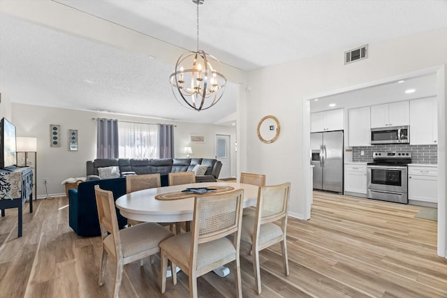 dining space with a chandelier, a textured ceiling, and light wood-type flooring