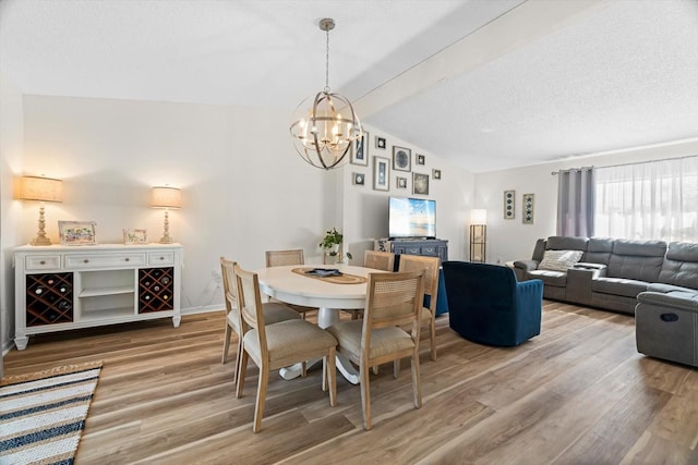 dining space with lofted ceiling with beams, wood-type flooring, a textured ceiling, and an inviting chandelier