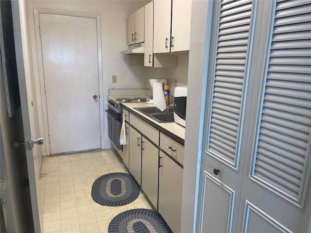 kitchen with electric stove, light tile patterned floors, and white cabinetry