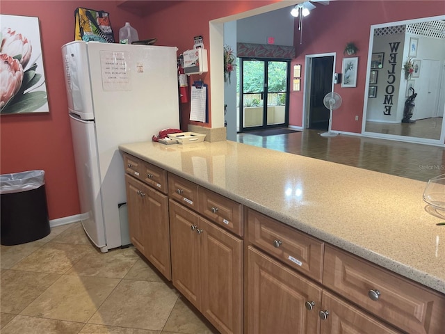 kitchen with light stone counters, light tile patterned flooring, and white fridge