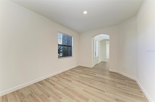 unfurnished room featuring arched walkways, baseboards, light wood finished floors, and recessed lighting