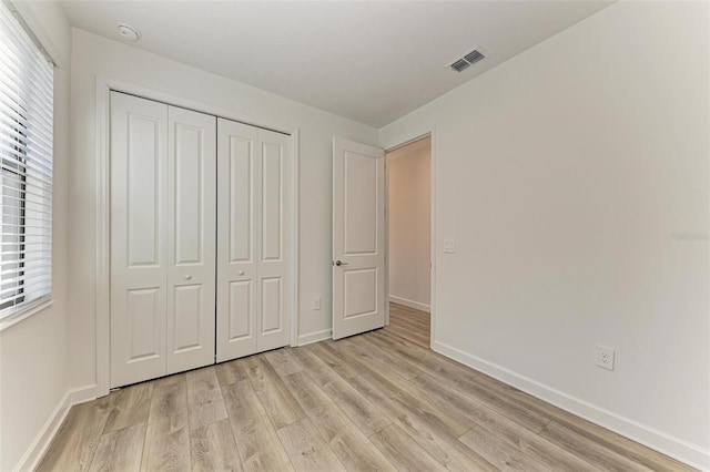 unfurnished bedroom with light wood-type flooring, baseboards, visible vents, and a closet