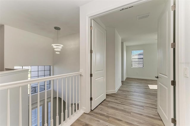 hallway with a notable chandelier, visible vents, baseboards, an upstairs landing, and light wood-style floors