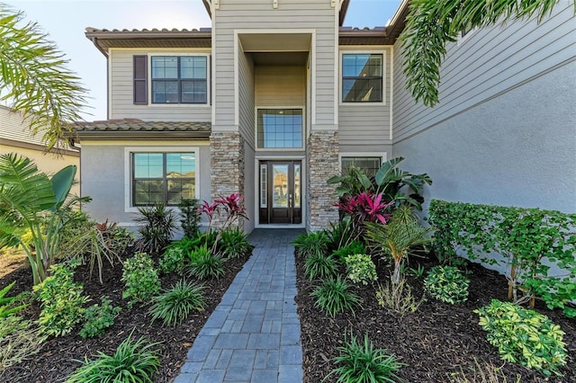 doorway to property with stone siding, a tiled roof, and stucco siding