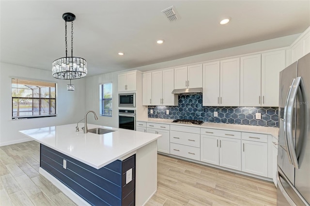 kitchen featuring light countertops, appliances with stainless steel finishes, white cabinets, a sink, and an island with sink