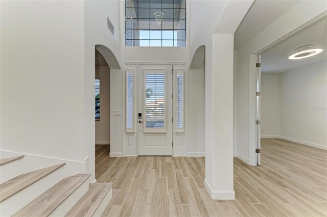 foyer featuring arched walkways, baseboards, visible vents, and light wood finished floors