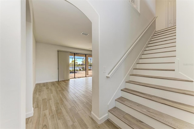 stairway with arched walkways, visible vents, baseboards, and wood finished floors