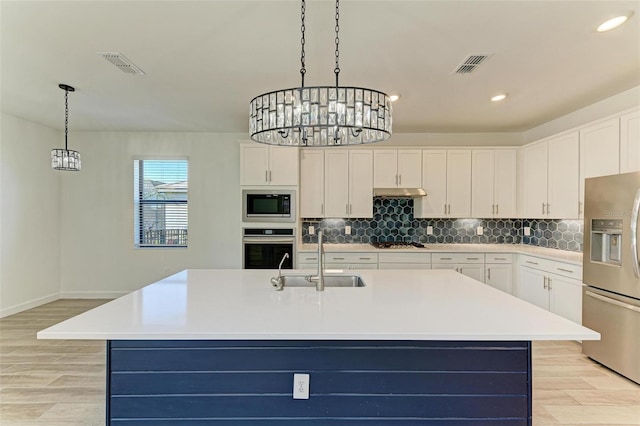 kitchen featuring stainless steel appliances, light countertops, a sink, and an island with sink