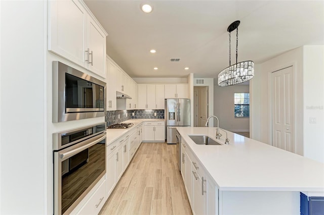 kitchen featuring appliances with stainless steel finishes, white cabinetry, a sink, and an island with sink