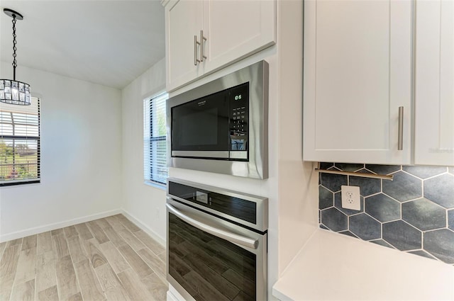 kitchen with black microwave, oven, white cabinetry, light wood-type flooring, and decorative light fixtures