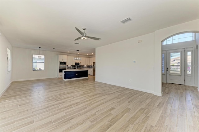 unfurnished living room with light wood finished floors, plenty of natural light, visible vents, and ceiling fan