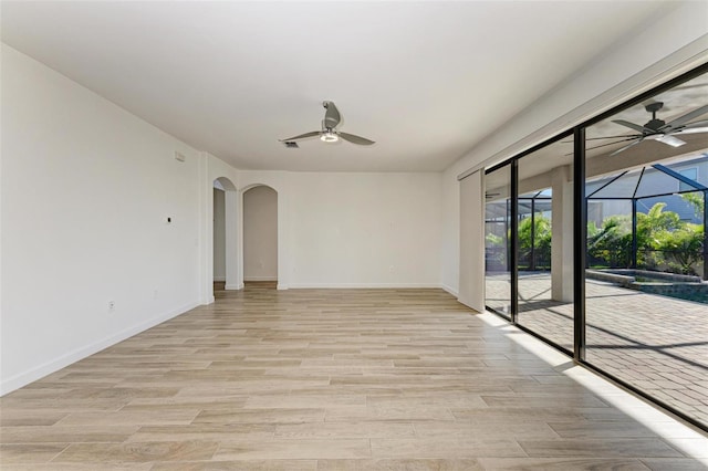 empty room featuring arched walkways, ceiling fan, light wood-style flooring, and a sunroom