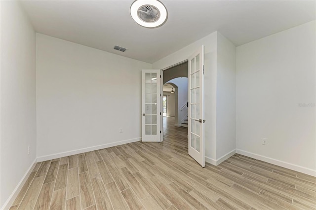 unfurnished room with light wood-style floors, arched walkways, french doors, and visible vents