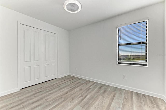 unfurnished bedroom featuring light wood-type flooring, a closet, and baseboards