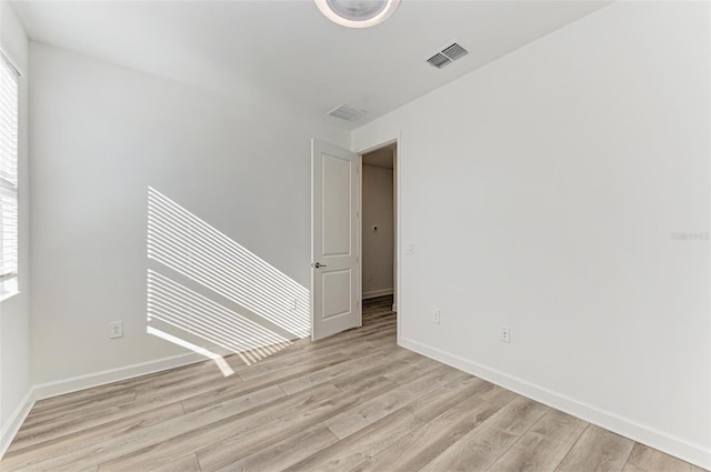 empty room featuring light wood-style flooring, visible vents, and baseboards