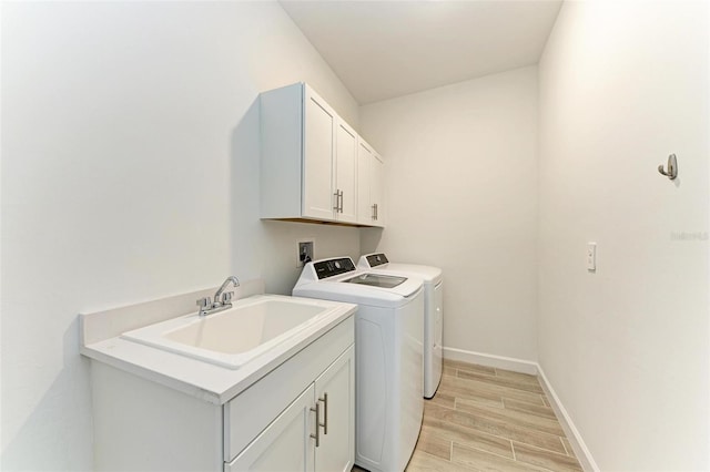 clothes washing area featuring wood finish floors, a sink, baseboards, cabinet space, and washer and clothes dryer