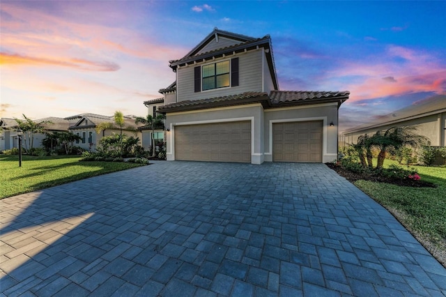 view of front of property featuring decorative driveway, a tile roof, stucco siding, a lawn, and an attached garage