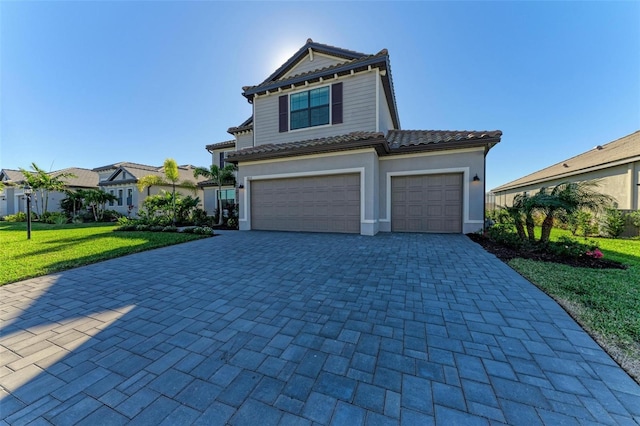 view of front of house featuring a garage, a tile roof, decorative driveway, a front yard, and stucco siding