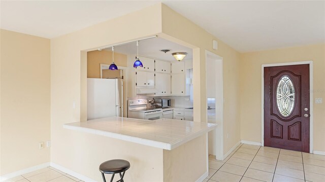 kitchen featuring a breakfast bar, white cabinets, light tile patterned floors, kitchen peninsula, and white appliances