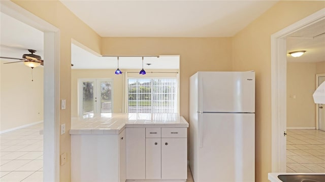 kitchen with white cabinetry, tile countertops, light tile patterned floors, white fridge, and pendant lighting