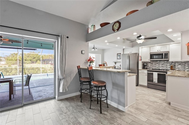 kitchen featuring a breakfast bar, backsplash, stainless steel appliances, white cabinets, and kitchen peninsula