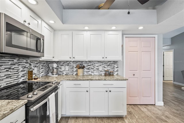 kitchen with backsplash, stainless steel appliances, light stone counters, white cabinets, and light wood-type flooring