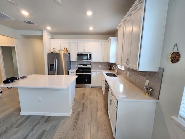 kitchen featuring sink, backsplash, stainless steel appliances, white cabinets, and a kitchen island