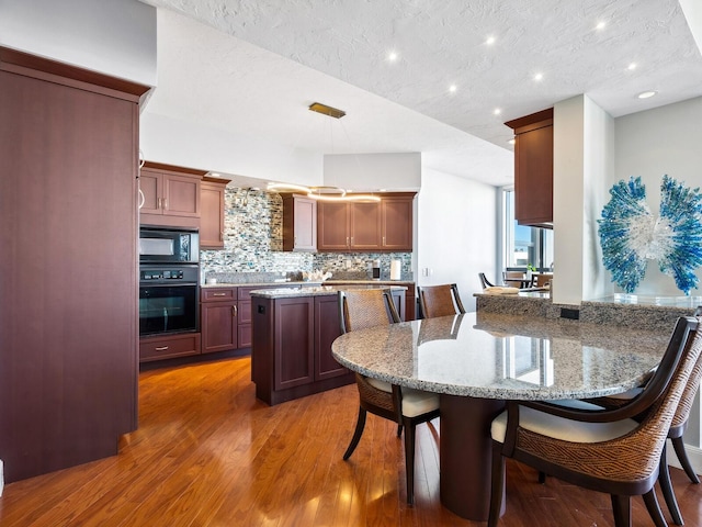 kitchen with decorative light fixtures, dark hardwood / wood-style flooring, decorative backsplash, light stone counters, and black appliances