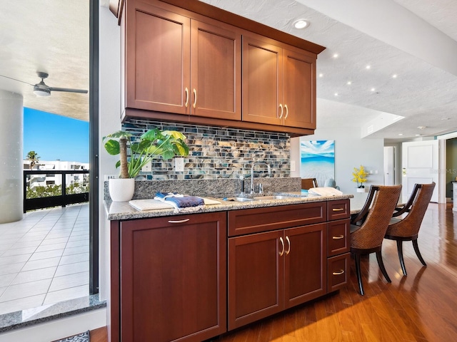 bar featuring tasteful backsplash, sink, light stone counters, and light hardwood / wood-style flooring