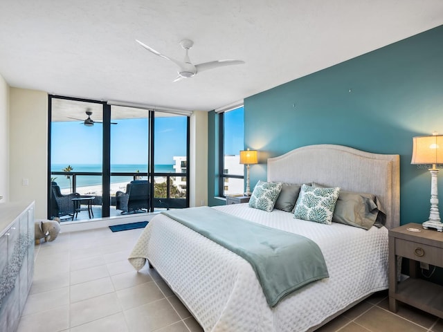 tiled bedroom featuring a water view, ceiling fan, and a wall of windows