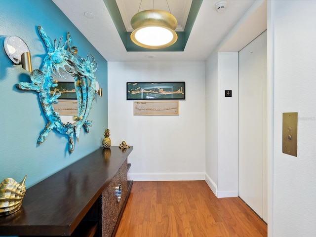 hall with hardwood / wood-style flooring, elevator, and a raised ceiling